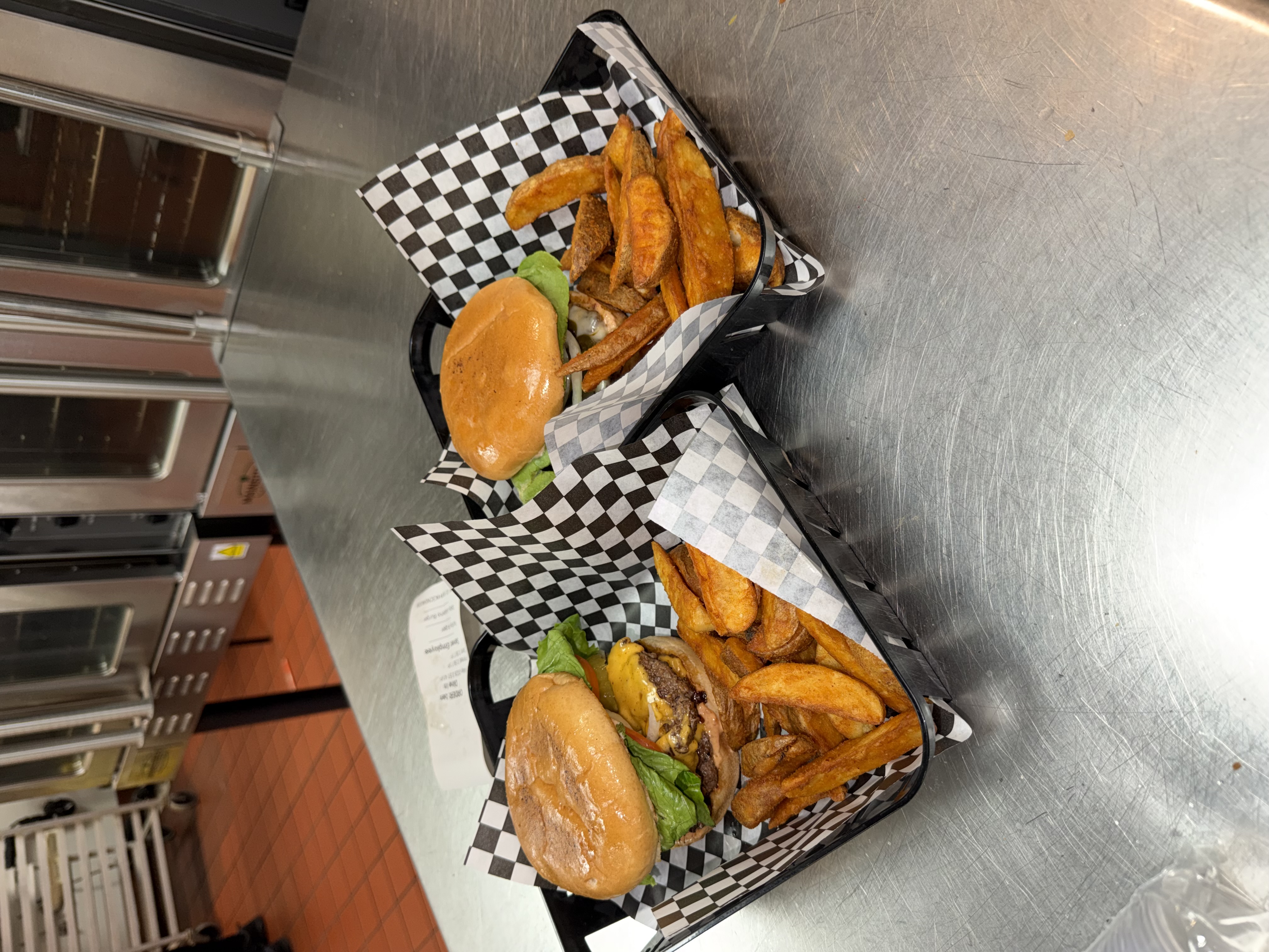 Two cheeseburgers with lettuce and tomato served in baskets with hand-cut wedge fries