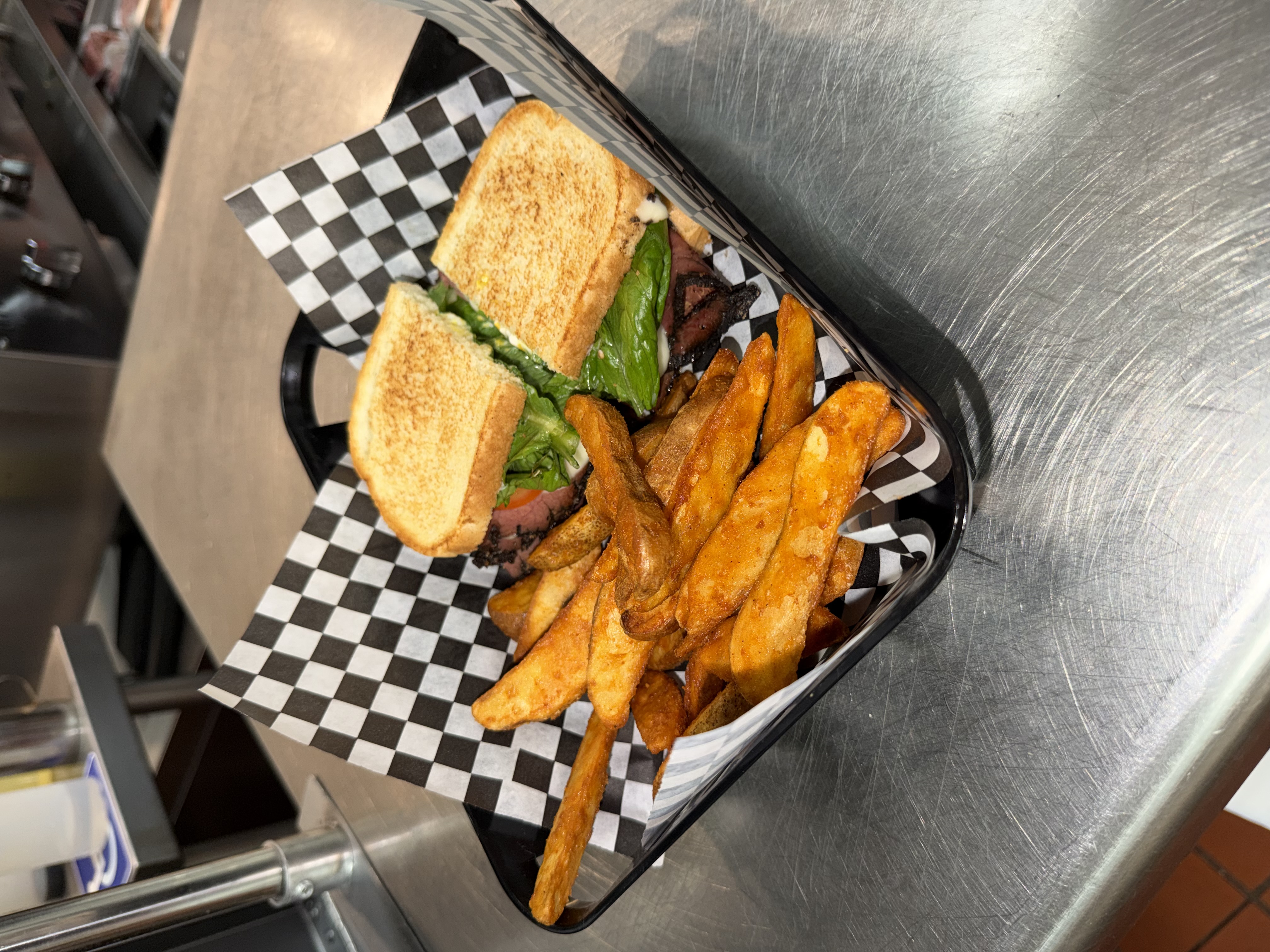 Hot pastrami sandwich on toasted bread with a basket of seasoned wedge fries